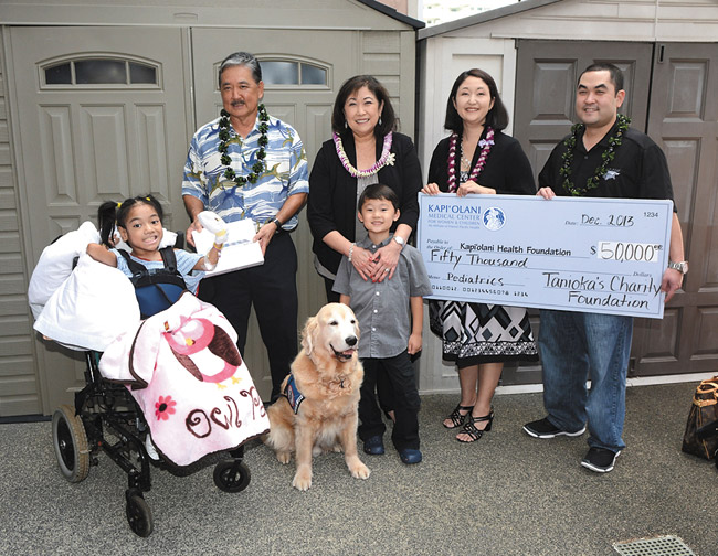 Fololesia Likio (left), a 10-year-old patient at Kapiolani Medical Center for Women and Children, accepts an iPad gift from Suehiro Electric and Tanioka's Seafoods and Catering. Also pictured (from left) are Mel Tanioka, Tucker (the hospital's chief canine officer), Lynn Tanioka, Ethan Lum, Jasmine Tanioka-Lum and Justin Tanioka. Photo courtesy of ACESxp.