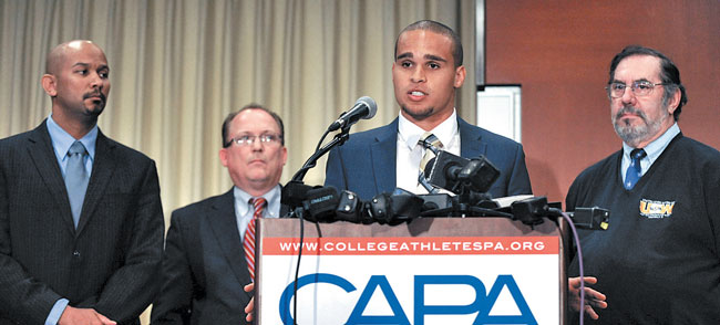 Kain Colter (at podium) speaks about unionizing players at a Jan. 28 news conference in Chicago, while College Athletes Players Association president Ramogi Huma (left), United Steel Workers national political director Tim Waters (second from left), and United Steel Workers president Leo Gerard look on | AP Photo/Paul Beaty