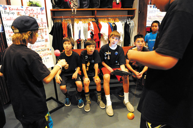 Luke and Logan Henderson (sitting at left) watch as participants perform tricks at their recent kendama tournament | Nathalie Walker photo