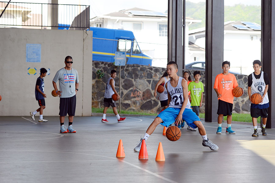 Coach Agena looks on as Logan Tanaka from Kalani High School practices drills.